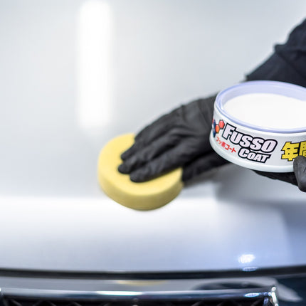 Dóza SOFT99 Fusso Coat v černých rukavicích, vedle žluté houby.