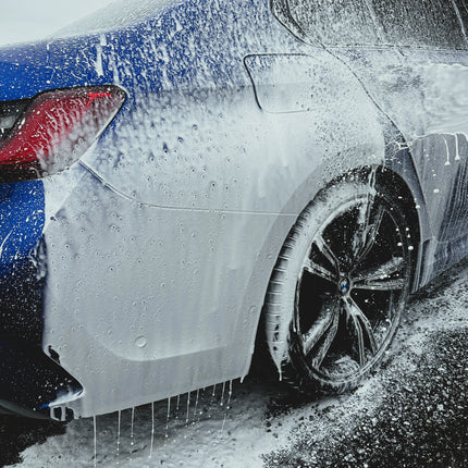 Bílá pěna pokrývající kapotu a okolí předního kola automobilu.