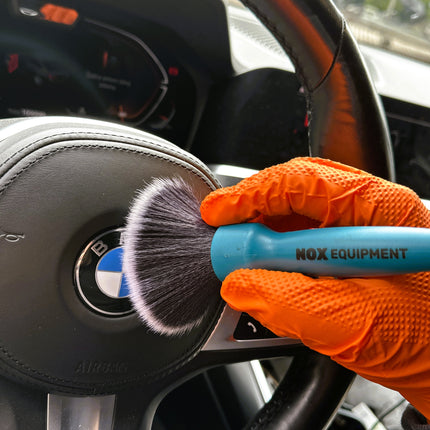 Dvojitý štětec DualBrush v oranžových rukavicích čistí volant s černými štětinami