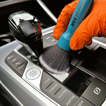 Dvojitý štětec DualBrush v oranžových rukavicích čistí řadicí páku černými štětinami